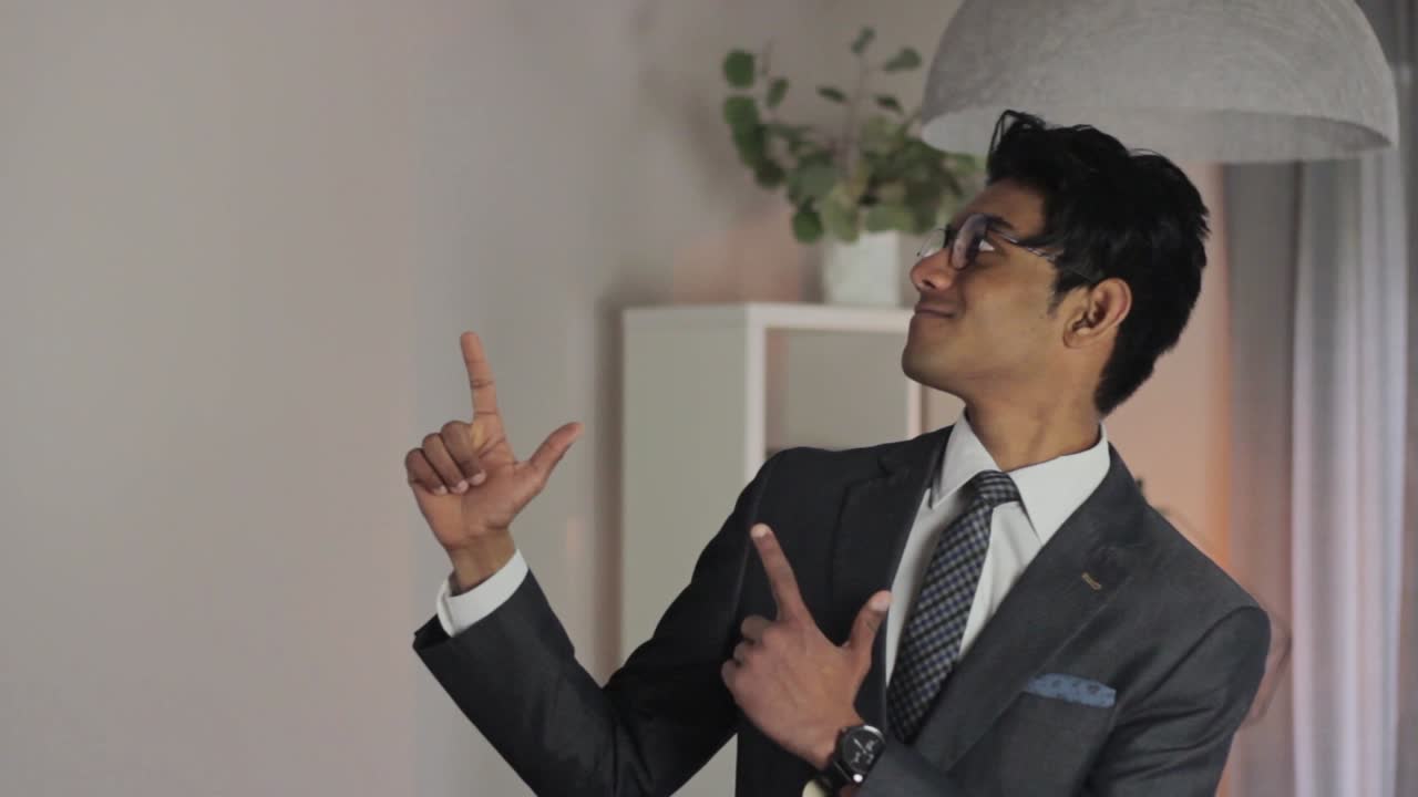 전문적으로 옷을 입은 남자가 손가락 총을 만들고 고개를 끄덕이며 측면을 바라보고 있습니다.