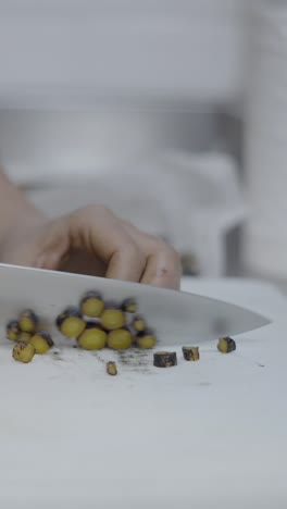 close-up of a hand chopping small yellow ingredients with a knife on a cutting board