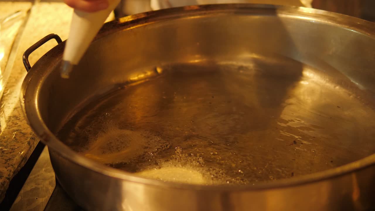 Primo piano di uno chef che frigge ciambelle in una grande padella nella cucina dell'hotel