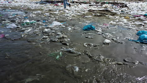 la costa arenosa del océano cubierta de montones de plástico mientras una joven y hermosa mujer camina