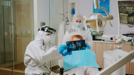 médico en traje de protección discutiendo sobre la radiografía del diente con la madre del niño