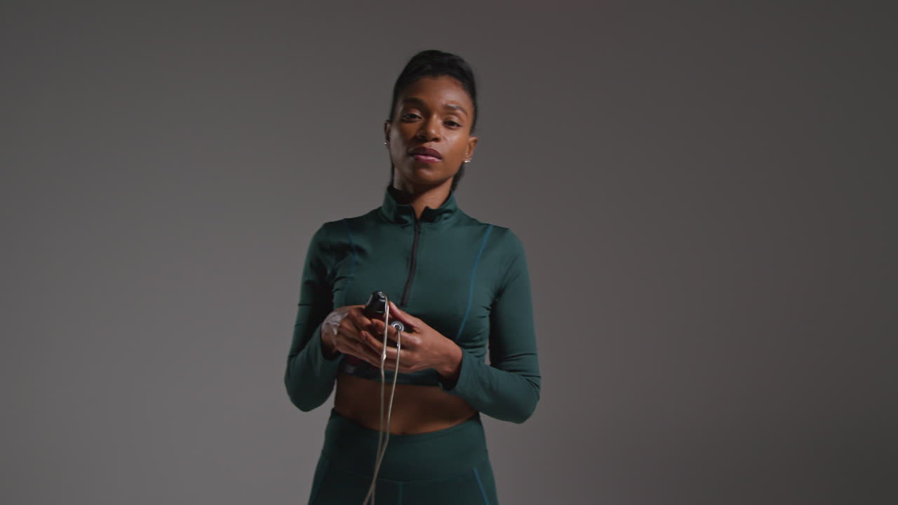 retrato de estudio de una atleta que usa un traje de entrenamiento en una clase de gimnasia con una cuerda para saltar o una cuerda de salto contra un fondo plano