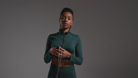 Studio-Portrait-Of-Female-Athlete-Wearing-Tracksuit-Training-In-Gym-Fitness-Class-With-Jump-Rope-Or-Skipping-Rope-Against-Plain-Background