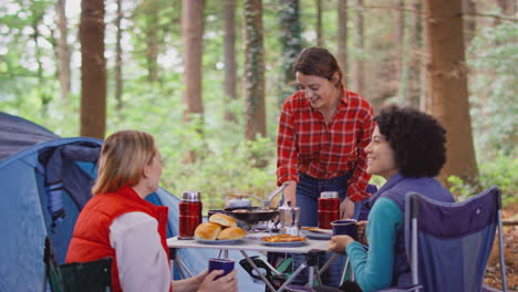 grupo de amigas en vacaciones de campamento en el bosque cocinando comida sentados en una tienda de campaña juntos