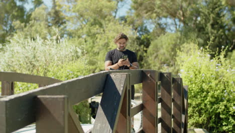 long shot of man standing on bridge with phone during cycling