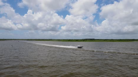 speedboat on a wide river with marshland under a cloudy sky