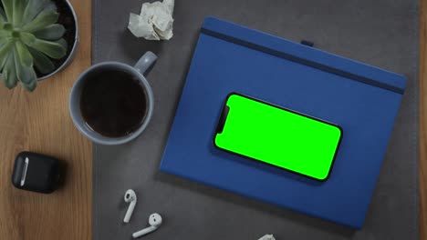 un teléfono móvil con una pantalla verde se encuentra en un bloc de notas en el primer plano del escritorio