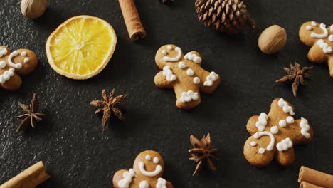 Video-of-smiling-gingerbread-men-and-spices,-slices-of-orange-and-nuts-over-black-background