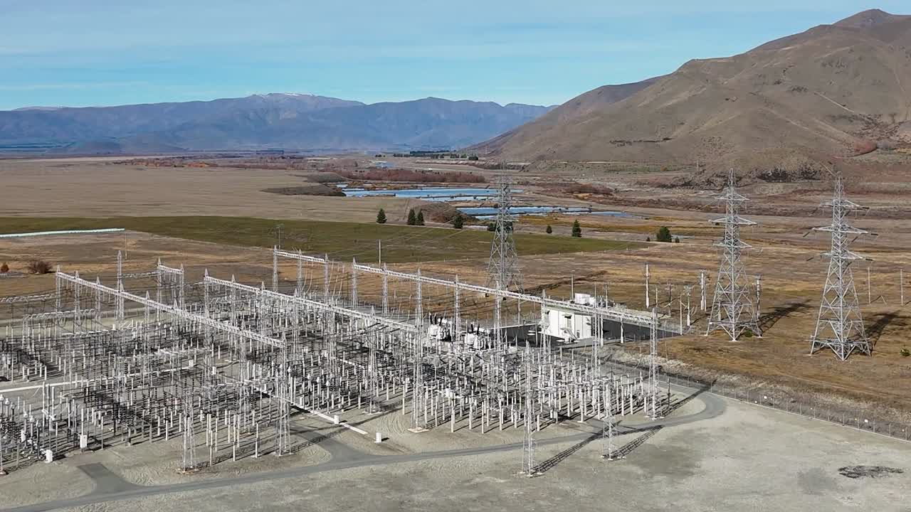Filmato aereo da drone con angolo di ripresa elevato che mostra un'infrastruttura di una sottostazione elettrica sullo sfondo di uno scenario montano suggestivo
