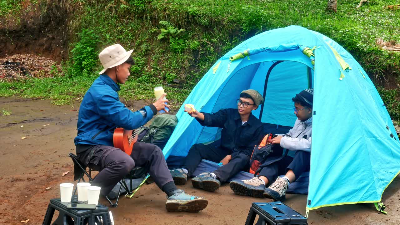 Friends enjoying camping adventure sharing drinks and music by tent in nature