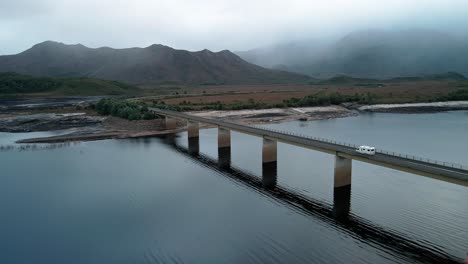 Forward-aerial-view-of-Lake-Burbury-with-vehicles-passing-through-bridge-in-Tasmania-,-Australia-on-a-foggy-day