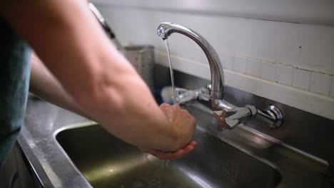 Joven-Lavándose-Las-Manos-En-El-Fregadero-De-La-Cocina-De-Plata