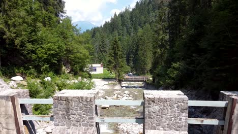 aerial dolly flying over a small dam downstream a creek flowing in a mountain forest