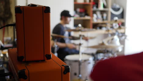 a drummer in a rock and roll garage band playing his instrument with guitar amps and music gear slow motion