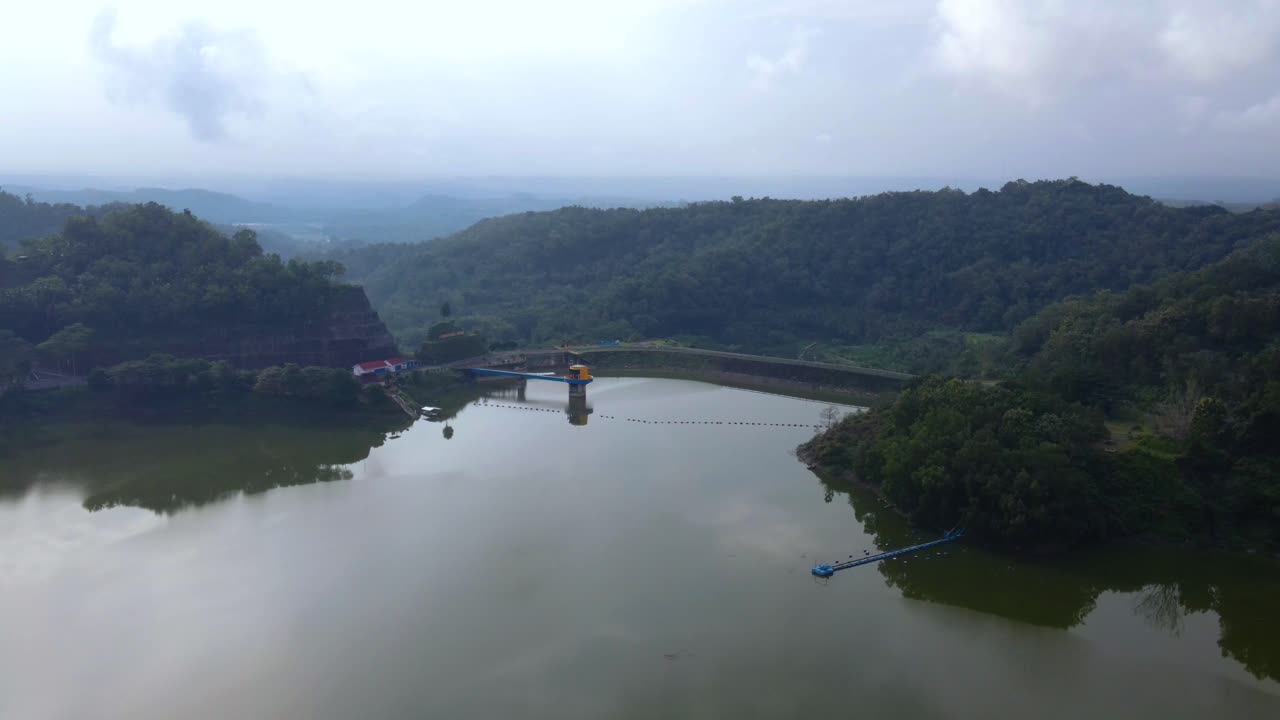 vista aérea del lago artificial construido en la colina que está rodeada de bosque en una mañana brumosa