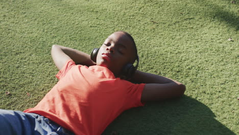 wearing headphones, boy relaxing on grass and enjoying music outdoors