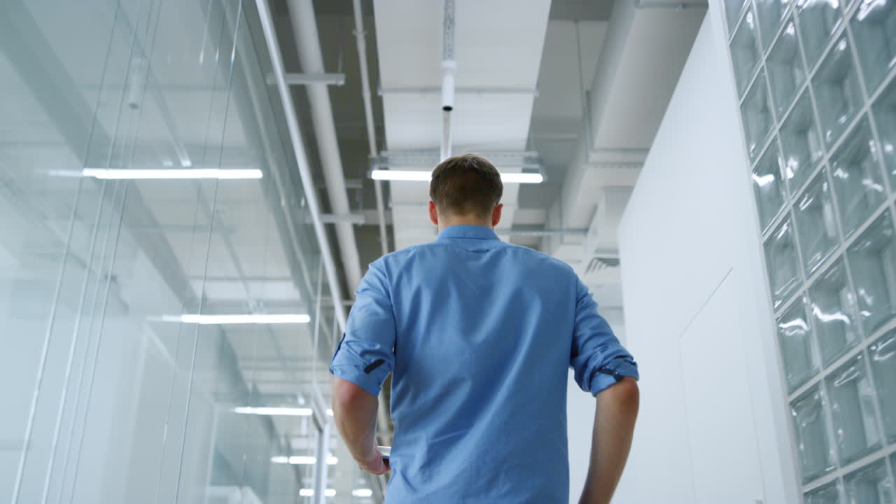 Empresário desconhecido caminhando com tablet por um espaço moderno. Homem observando o ambiente.