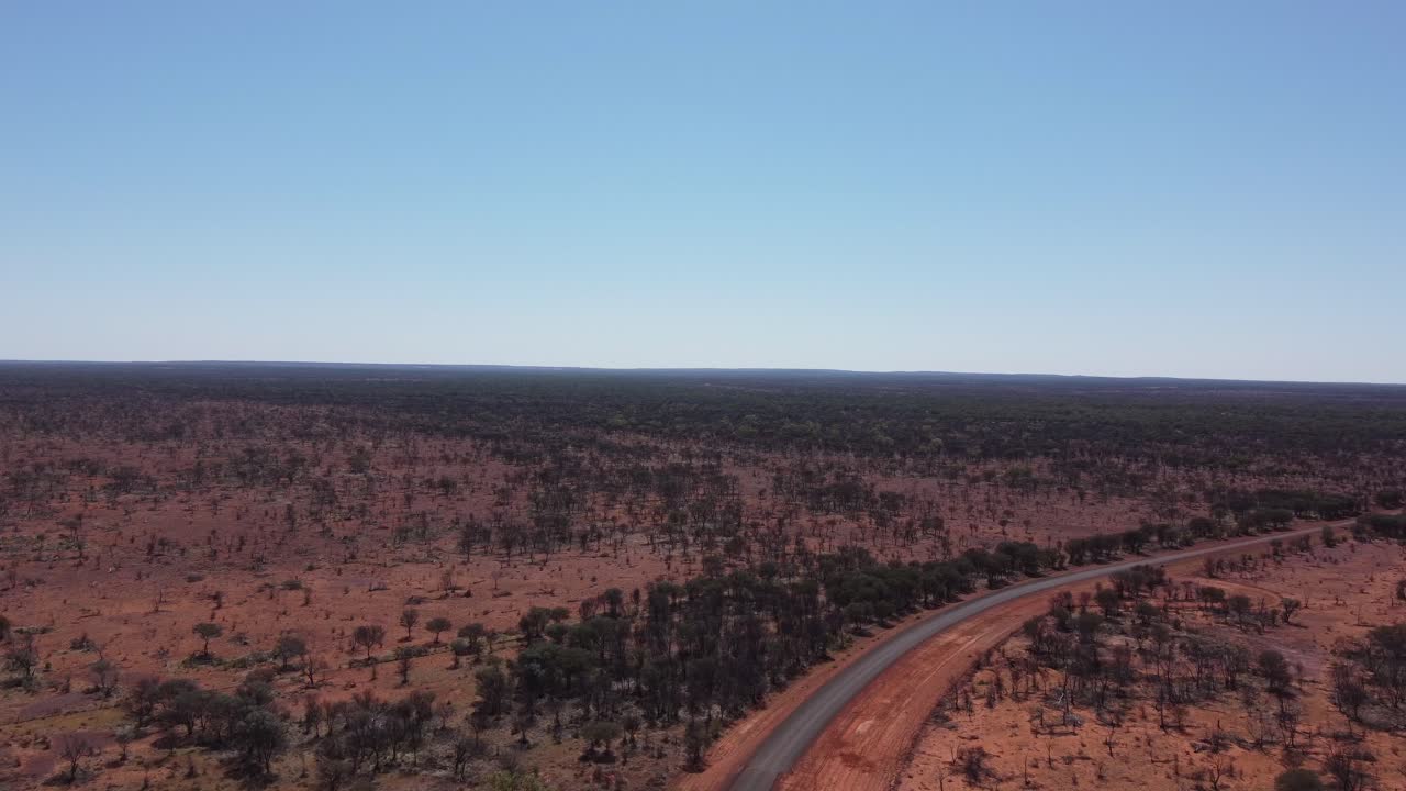 Drone terbang naik dan bergerak maju di atas jalan pedesaan beraspal di Outback Australia
