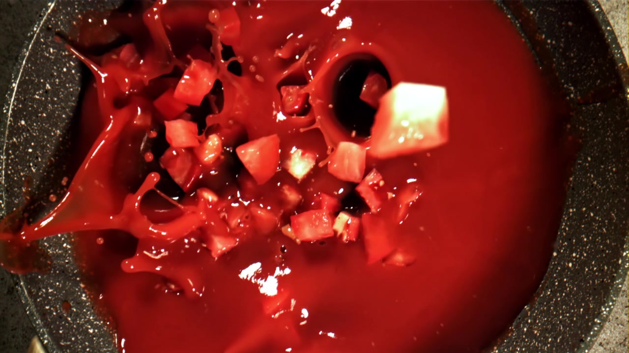 Pomodori a cubetti che cadono in sugo di pomodoro rosso in una padella al rallentatore