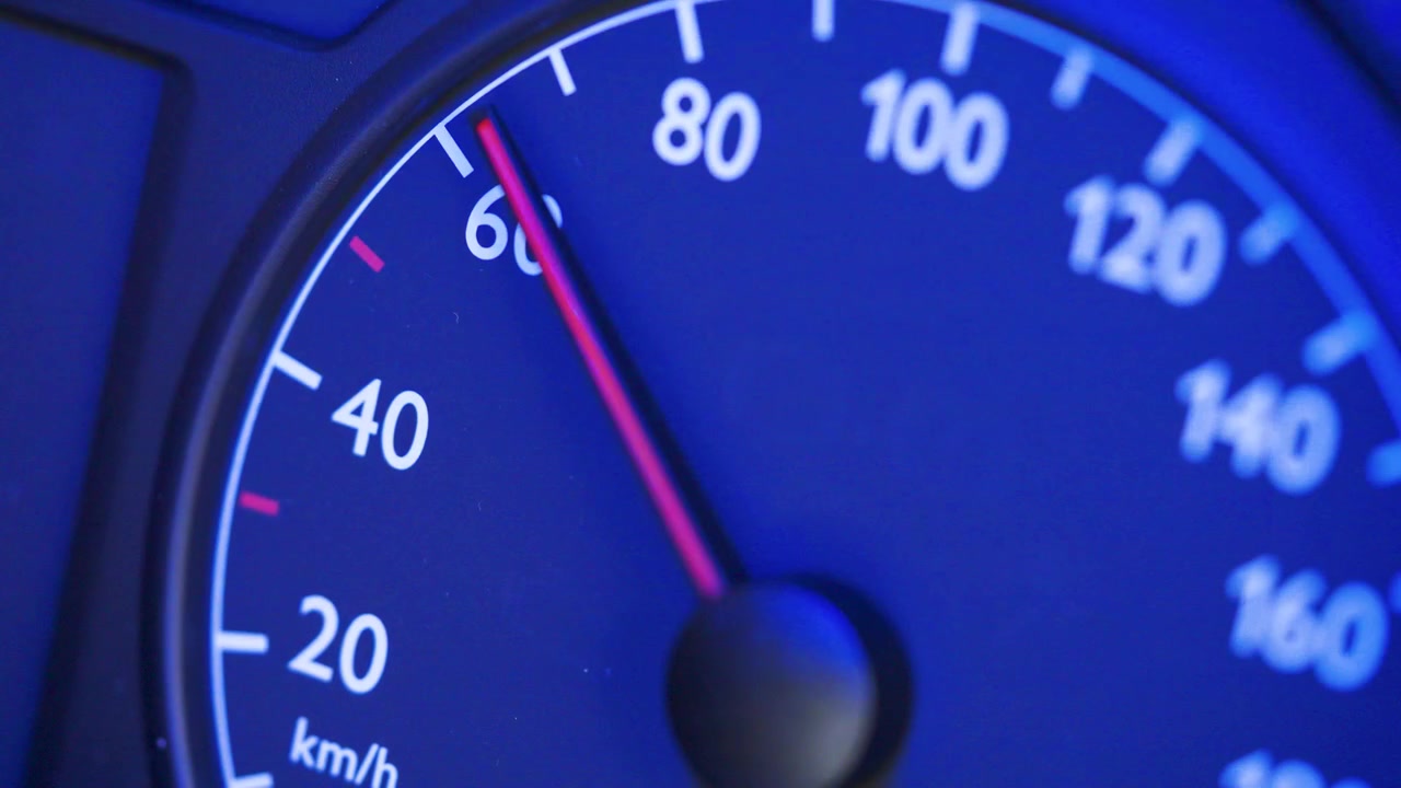 Close-up of a car speedometer showing 0 kmh with a red needle and blurred blue police lights in the background. Concept image for stopped vehicle, police control, traffic stop, road safety, law enfor