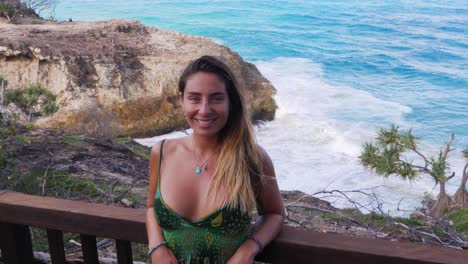 chica caucásica posando y sonriendo a la cámara - acantilado costero con olas rompiendo en el paseo del desfiladero norte, isla de stradbroke del norte, australia