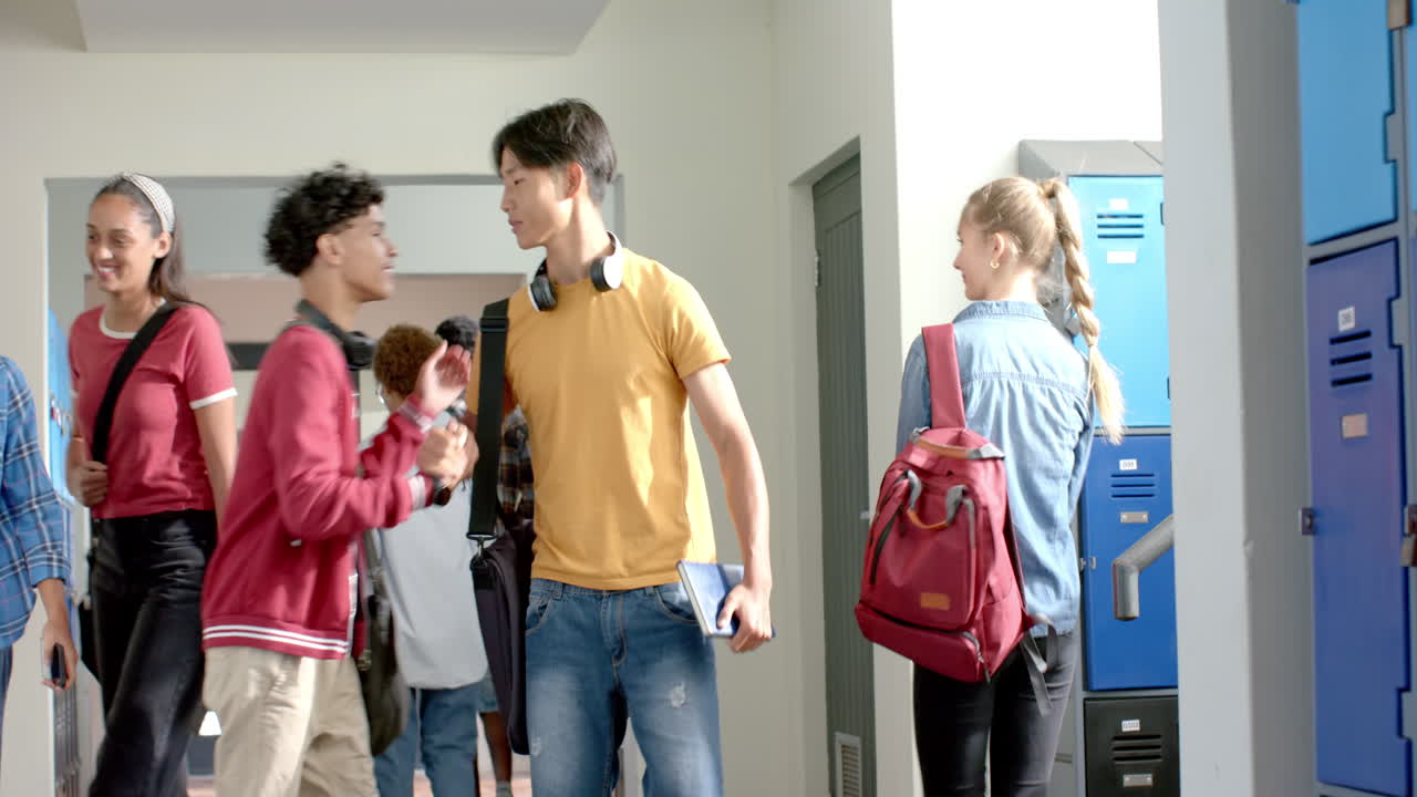 Teenagers in high school hallway talking and walking with backpacks and headphones