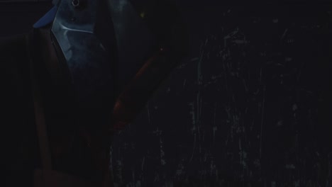 close-up of a welder illuminated by the welding arc, sparks flying around and hitting his welding helmet.