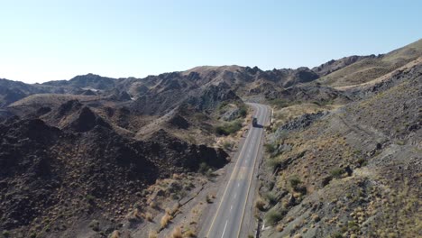 drone aéreo siguiendo el disparo sobre un camión que conduce a lo largo de una sinuosa carretera rcd rodeada por una cordillera en balochistán