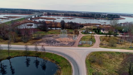 A-half-built-electrical-transmission-tower-pylon-along-a-countryside-road---aerial-view