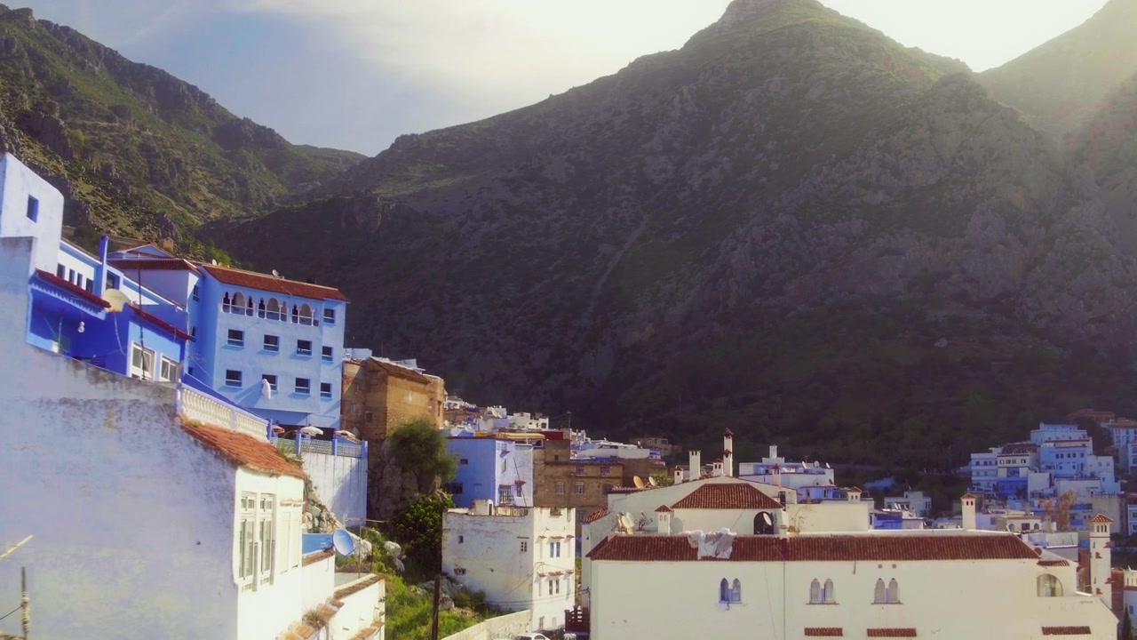 Il drone si alza tra gli edifici rivelando la medina blu di Chefchaouen e le montagne.