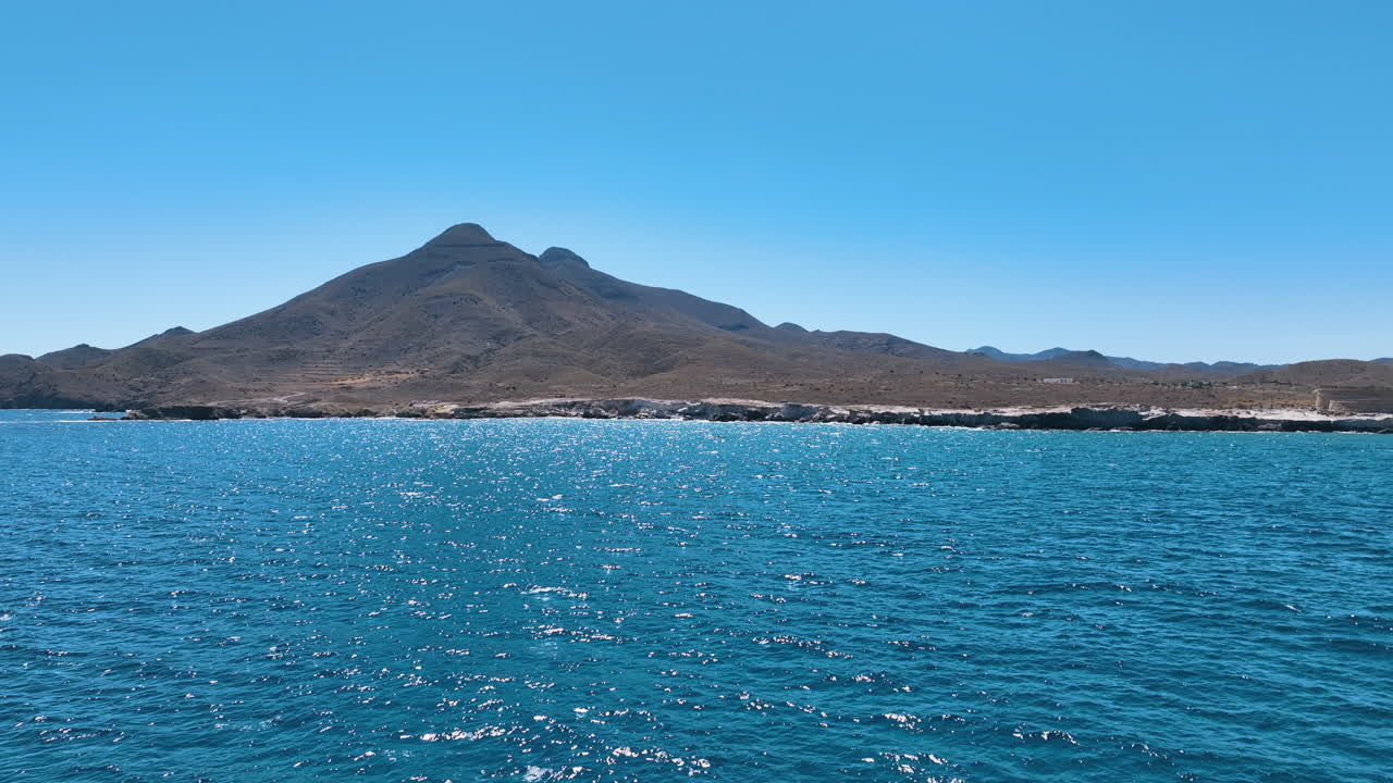 Aerial flies low over the dazzling blue Mediterranean waters under the looming beauty of the dramatic Los Frailes twin volcanoes in stark profile. Cabo de Gata Nijar National Park Almeria Andalusia