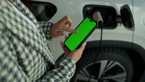 mujer usando el teléfono para cargar un coche eléctrico