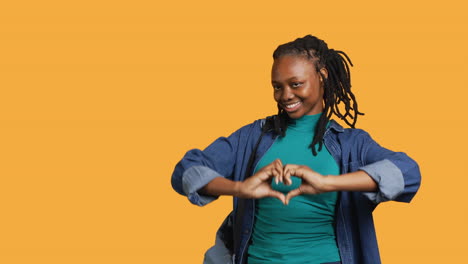 Portrait-of-affectionate-smiling-woman-doing-heart-symbol,-studio-background