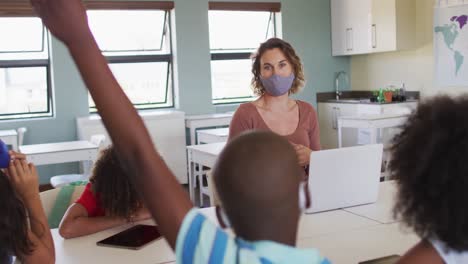 maestra que usa una máscara para la cara enseñando a los niños en la clase en la escuela