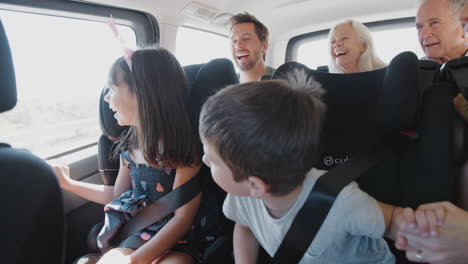 Multi-Generation-Family-Sitting-In-Back-Of-People-Carrier-Being-Driven-To-Vacation