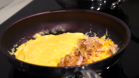 espátula agregando jamón cocido y cebollas a la tortilla de huevo - cocina en la estufa