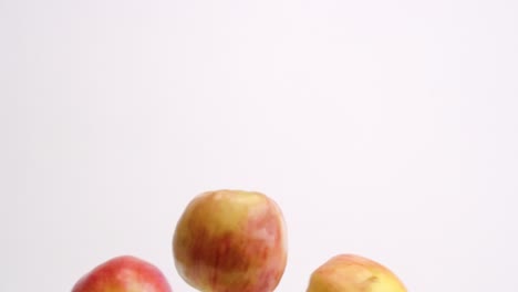 Red-and-yellow-fuji-apples-raining-down-on-white-backdrop-and-bouncing-up-and-down-in-slow-motion