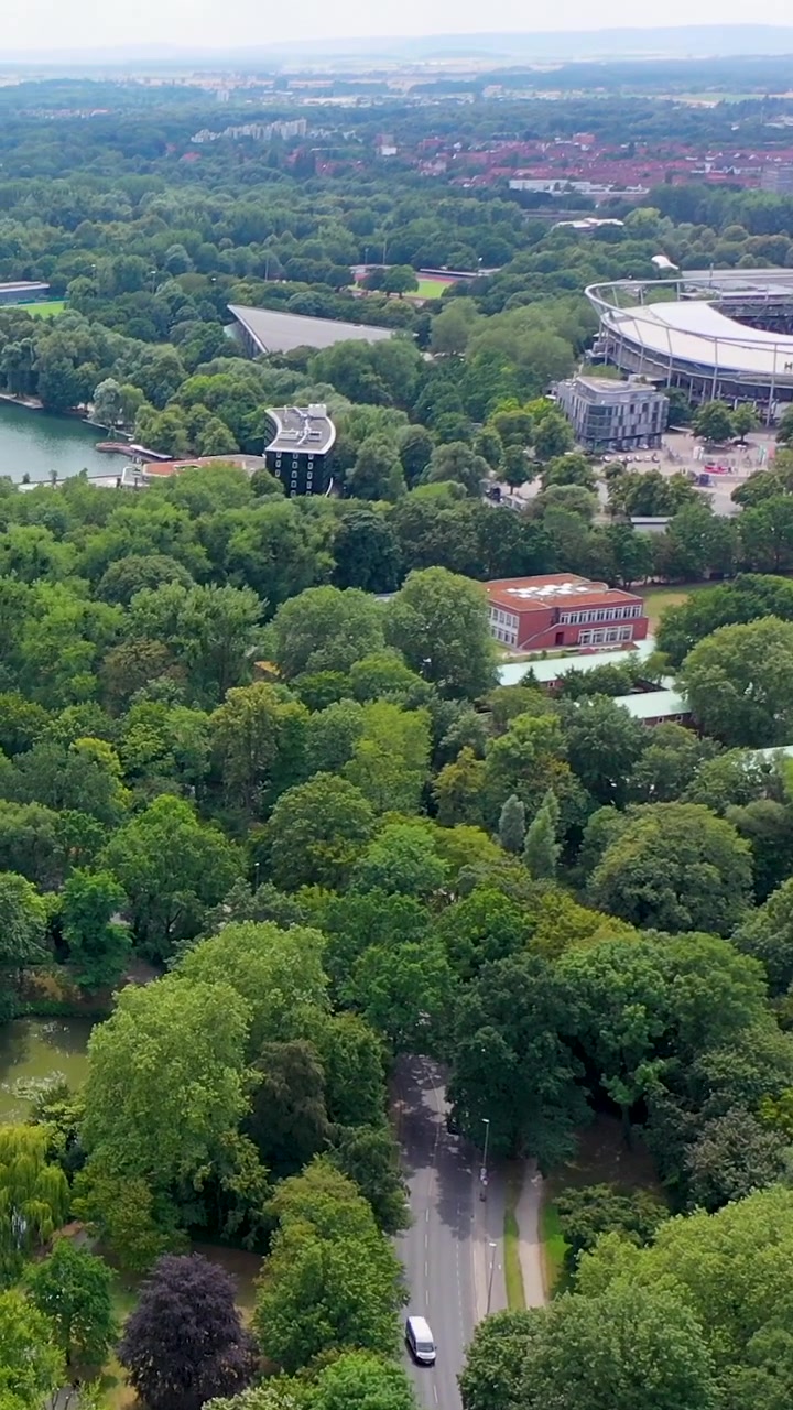Rekaman drone vertikal sinematik yang menghadap stadion Heinz von Heiden Arena yang dikelilingi pepohonan hijau rimbun dan taman kota di Hannover, Jerman