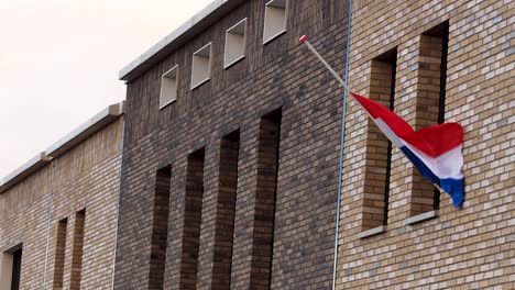 dutch national flag gently waving in the wind hanging half mast on the exterior facade of a modern building in commemoration of those fallen in war times