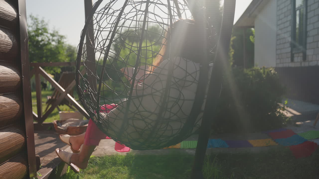 Woman Enjoys Peaceful Porch Evening, Woman Lounges In Sunny Garden Porch With Vibrant Cushions Present, Seated Female In Hanging Chair Basks Peacefully Under Warm Evening Sunlight In Garden