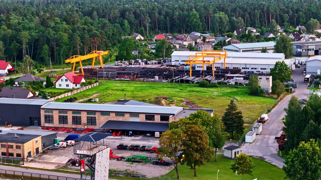 Aerial view of industrial metal pipe manufacturing facility with yellow cranes in residential area