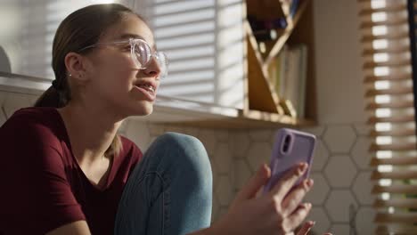 adolescente caucásica sentada en la cocina y haciendo una videollamada en el teléfono móvil