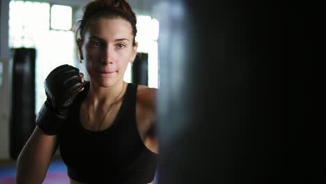 close up view of caucasian female boxer hitting the boxing bag with her hands in gloves in the gym alone. tough power training of