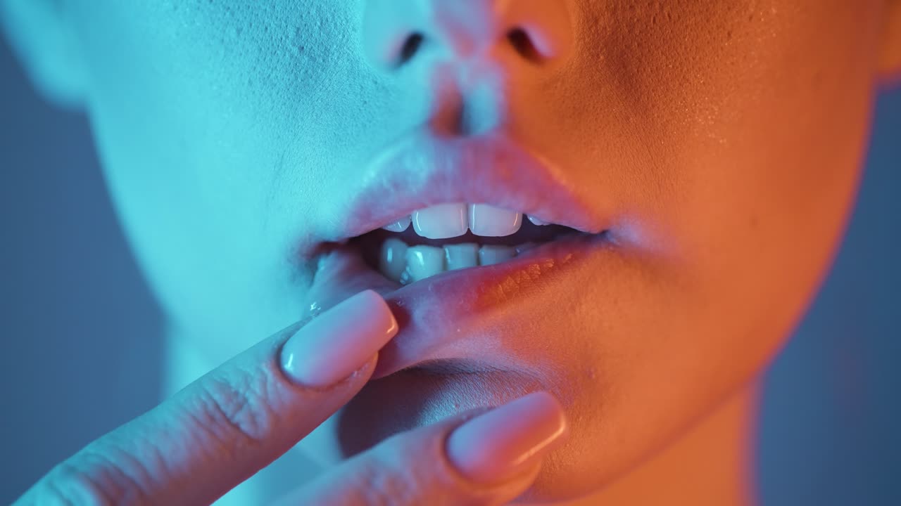 primer plano extremo de un hermoso labio de una mujer hermosa mientras la joven modelo acaricia sus labios seductoramente con sus dedos con contraste azul naranja en su cara en cámara lenta
