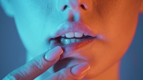 extreme close up of a lovely beautiful woman lip while the young model strokes her lips seductively with her fingers with blue orange contrast in her face in slow motion