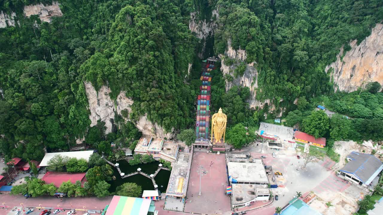 Drone udara mengitari pegunungan kapur besar Gua Batu di Kuala Lumpur Malaysia dengan tangga warna-warni menuju Patung Dewa Murugan pada sore berawan dan tanpa turis