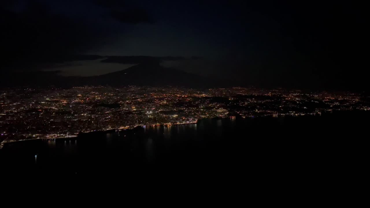 ночной вид на город катания в сицилии, снятый с высоты 1000 метров из кабины самолета, с очертаниями вулкана этна на заднем плане