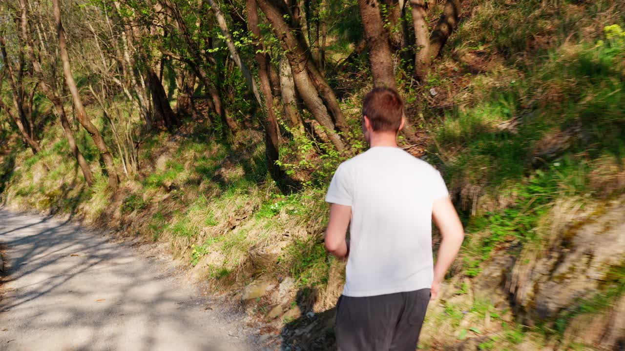 A young man runs along a forest path, enjoying nature and motion in the sunlight