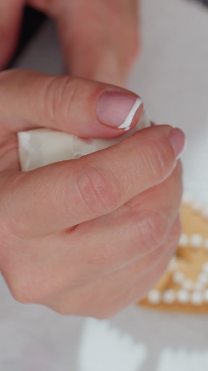 primer plano de una galleta de forma triangular decorada a mano con glaseado blanco de una bolsa de tubería, centrándose en pequeños puntos redondos de glaseado en papel blanco texturizado, con luz natural suave