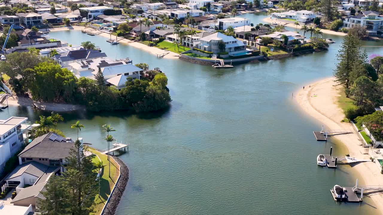 Drone glides above residential canal, modern waterfront houses, sunny weather, smooth cinematic movement